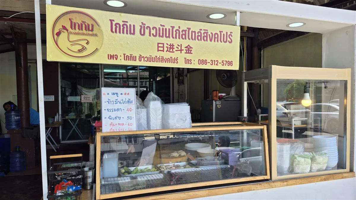 Front of Gokim Singapore-style chicken rice, Muak Lek: yellow sign, chicken display cabinet and the price menu board